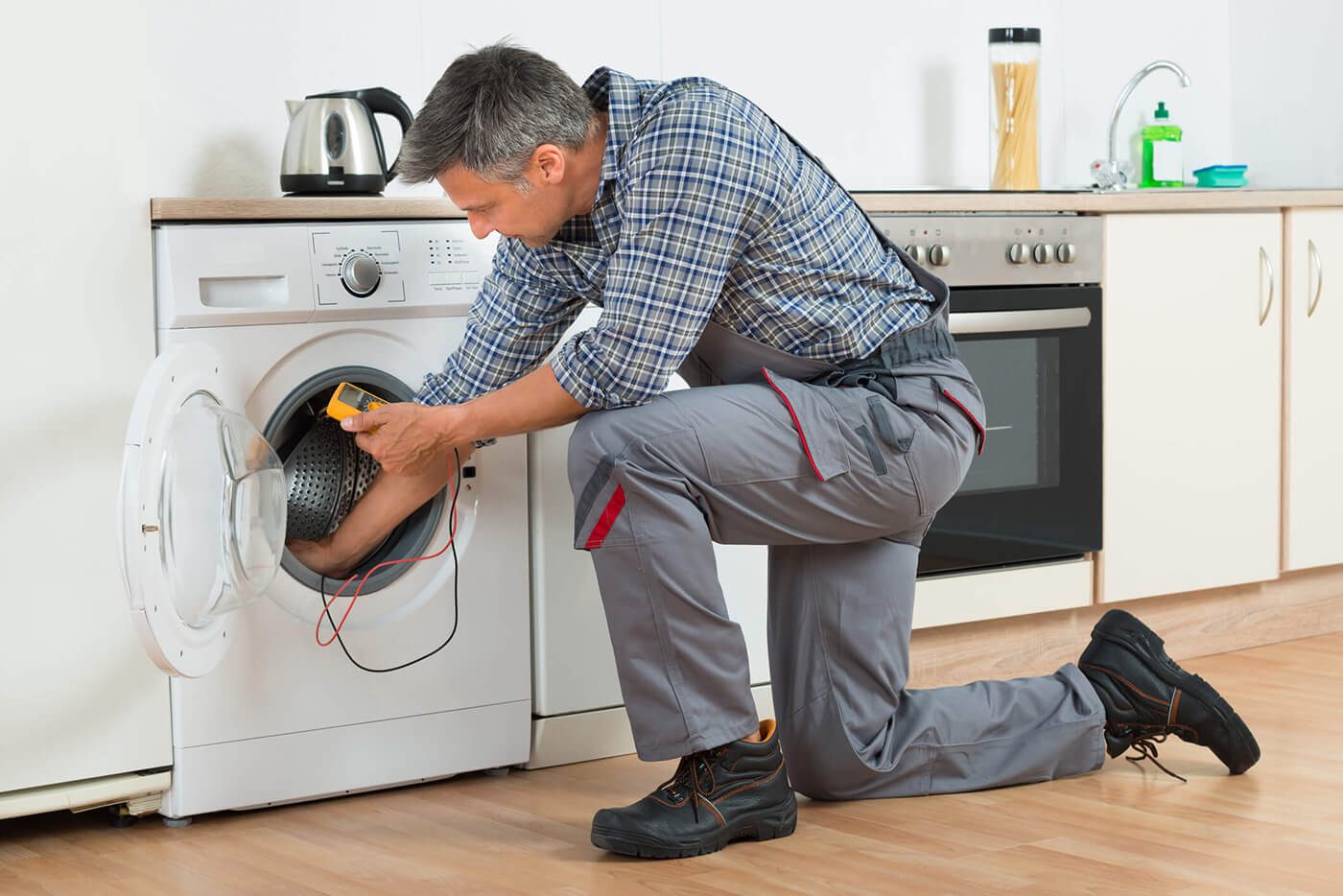 Technician kneeling at a front load washer with a meter in hand