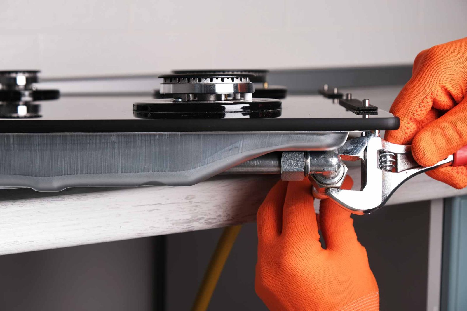 Close view of gloved hands adjusting a gas cooktop burner with a wrench
